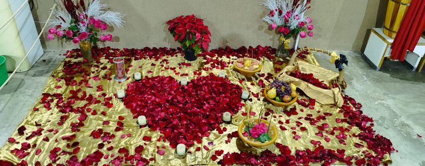 Altar decorado com pétalas, coração vermelho e frutas.